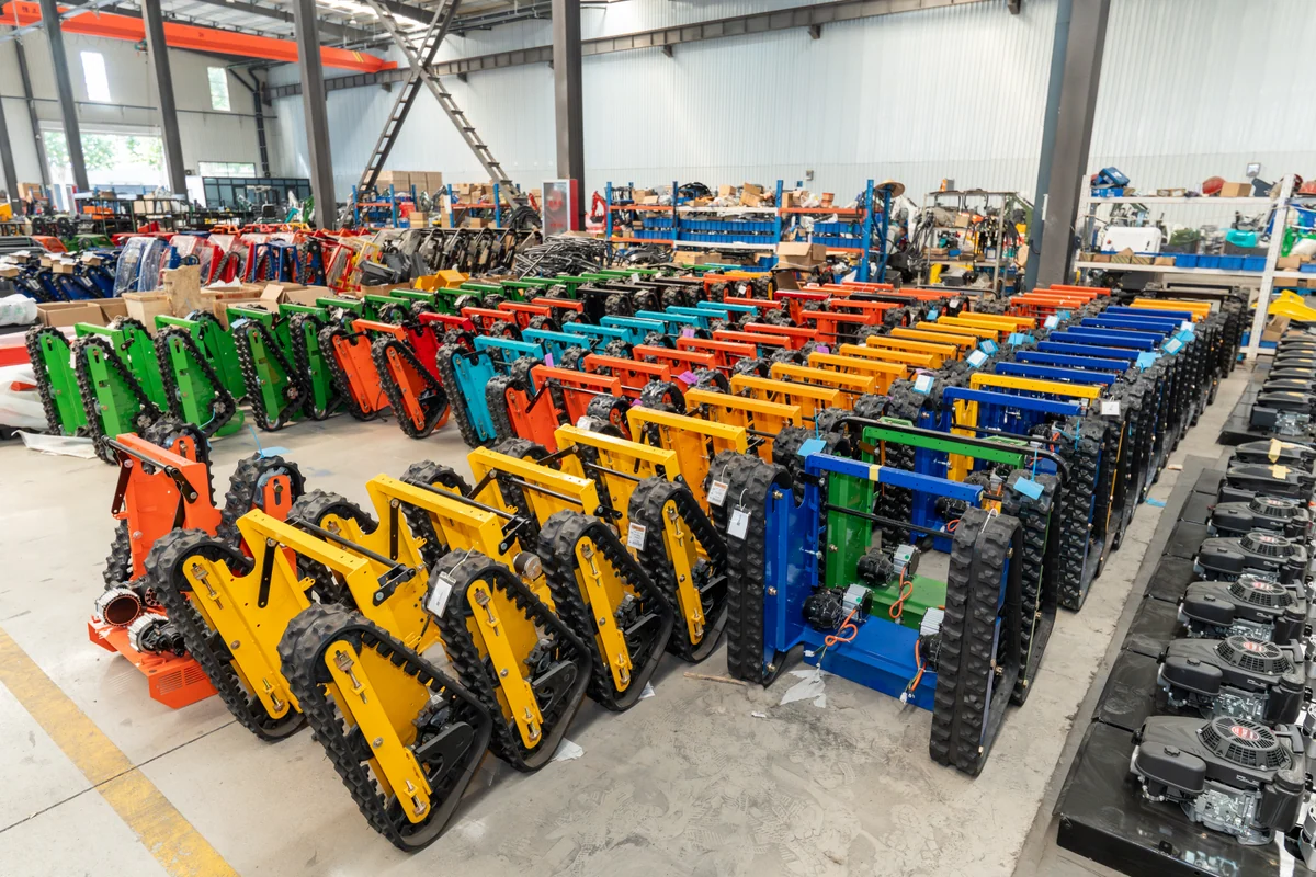Rows of tracked mower chassis in several colors inside the workshop.