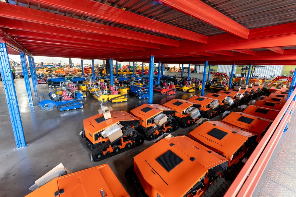 Orange mower units and tracked equipment arranged inside the factory workshop.